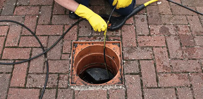 Drain cleaning technician using a drain snake to clear a clogged drain in Arlington, TX